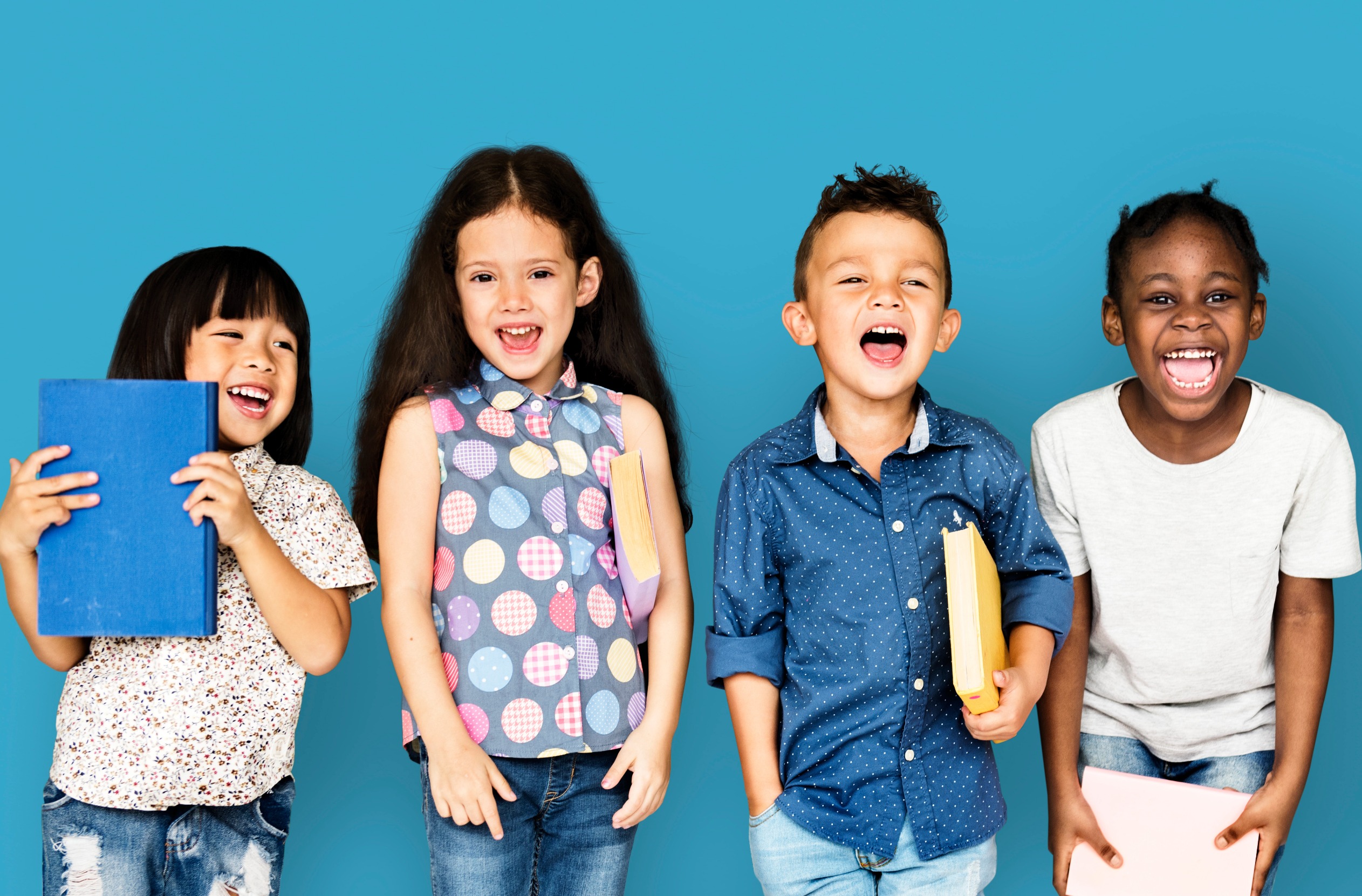 Image of four children standing in front of a blue background smiling and laughing. Discover how child therapy in Denver, CO can support your child and they challenges they may face.